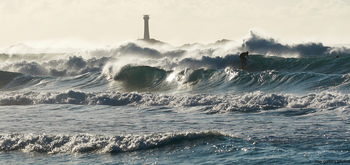 Surfing longships in heavy waves This landscape photograph, taken in the afternoon during the autumn season, depicts a surfer riding heavy waves off the coast of Sennen Cove in the United Kingdom. The sea is turbulent, with large waves dominating the scene, showcasing the raw power of nature. In the background, the iconic Longships Lighthouse stands tall on the horizon, marking a well-known landmark off the Cornish coast. The image captures the dynamic interaction between the surfer and the relentless waves, set against the dramatic backdrop of the open sea. The scene is quintessential of the United Kingdom's rugged coastline, with the Longships Lighthouse providing a focal point that highlights the maritime heritage of the area. The combination of the powerful waves, the lighthouse, and the coastal landscape emphasizes the natural beauty and challenging conditions that make this area popular for surfing.
